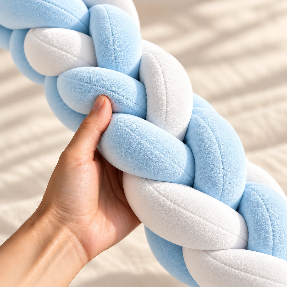 Tour de lit bébé tressé bleu ciel et blanc tenu en main pour montrer son moelleux