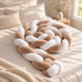 Tour de lit bébé tressé caramel et blanc, enroulé en spirale sur un lit