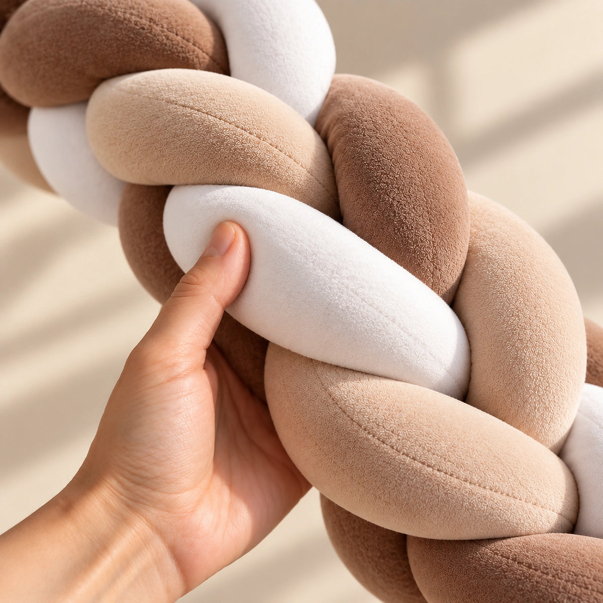 Tour de lit bébé tressé caramel et blanc tenu en main pour montrer son moelleux