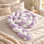 Tour de lit bébé tressé lilas et blanc, enroulé en spirale sur un lit